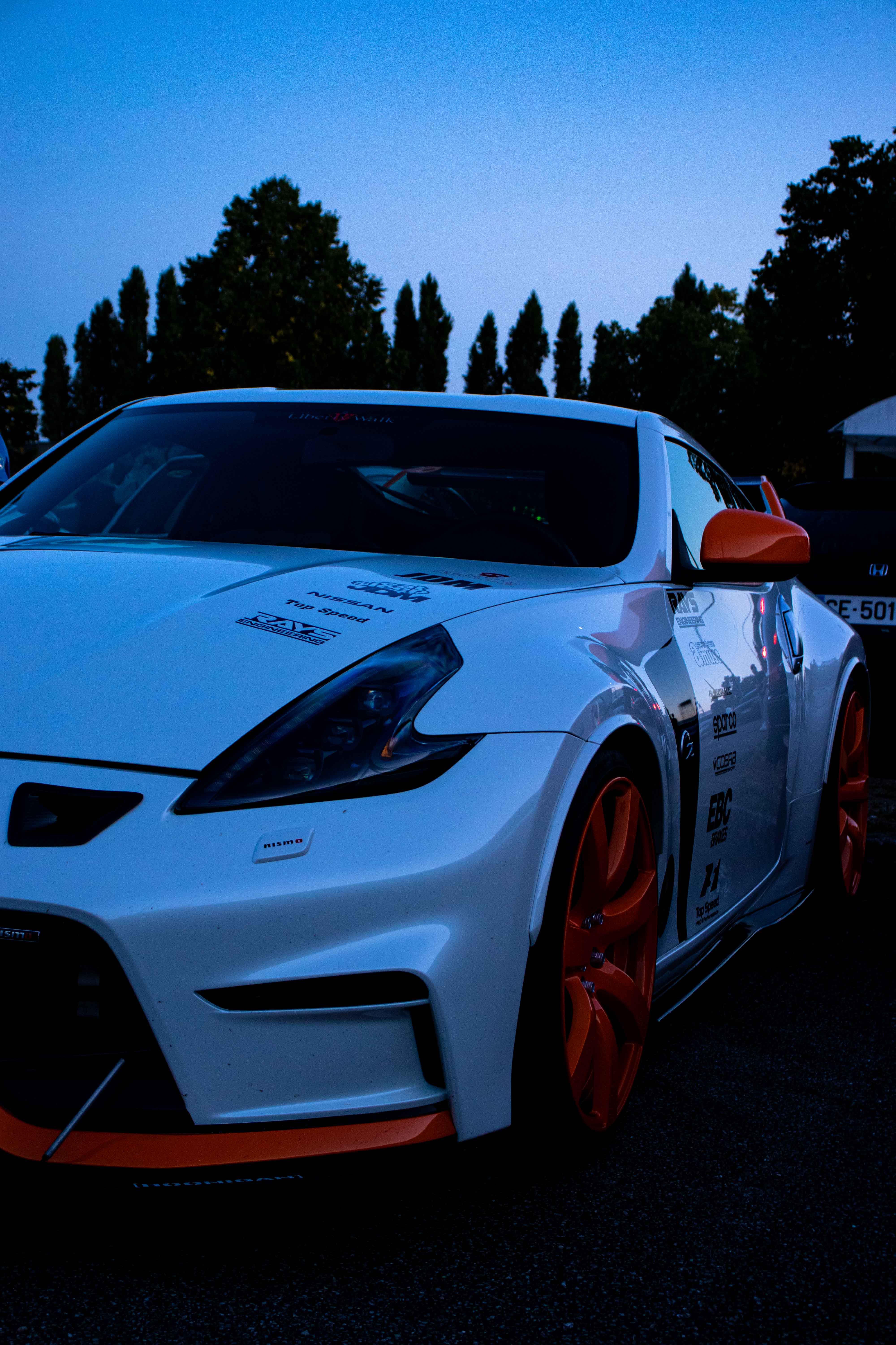Photo d'une voiture blanche et orange, centré sur le phare avant gauche